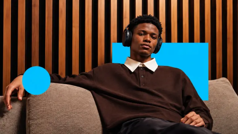 A young man in headphones relaxing on a sofa, with bright blue graphic shapes